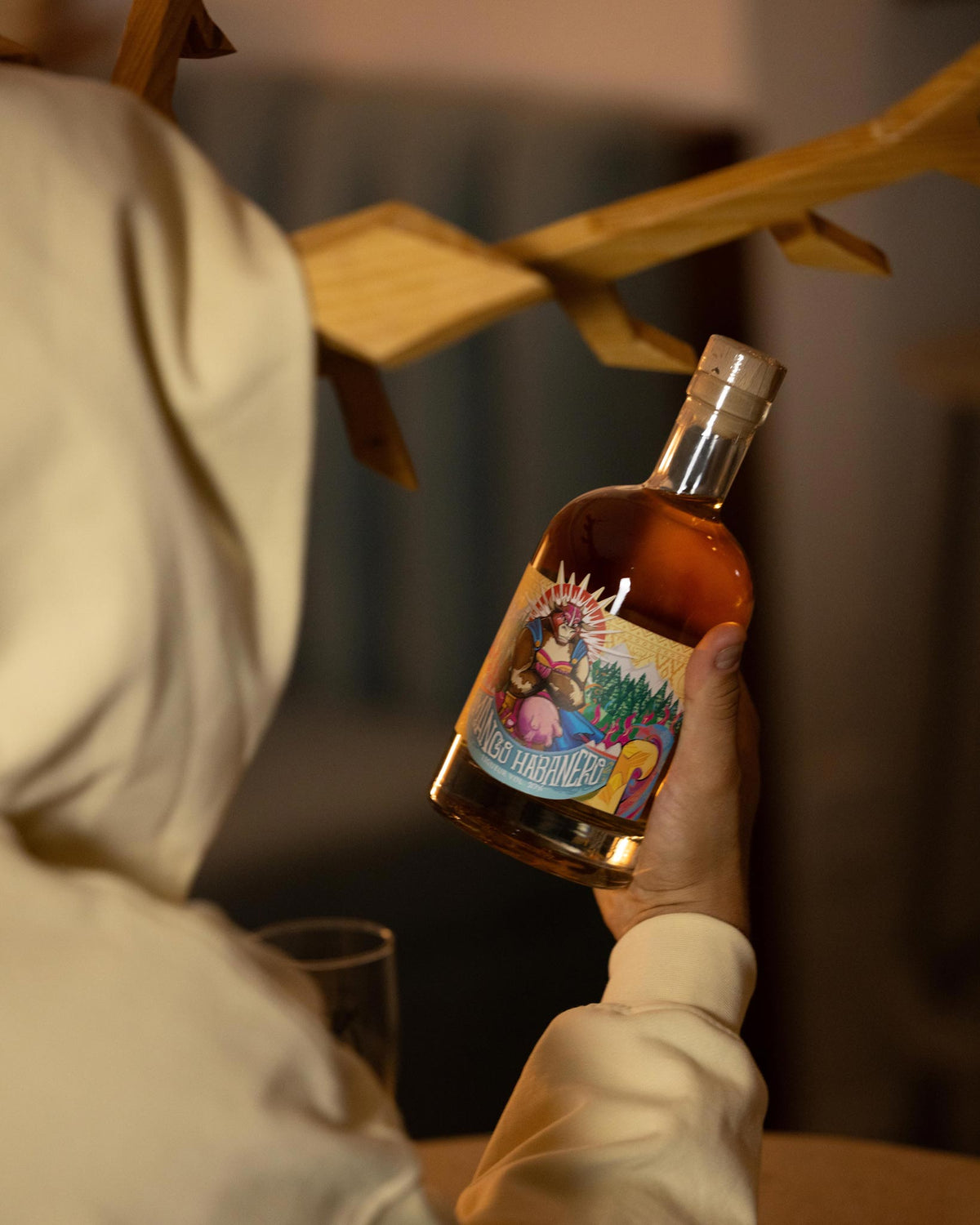 Person holding a bottle of MaHa Shot mango habanero liqueur next to a glass in warm bar light